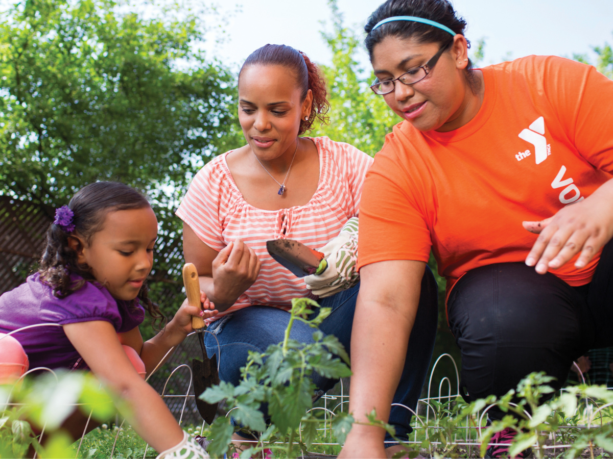 Two older adult women and a young girl plant a garden.