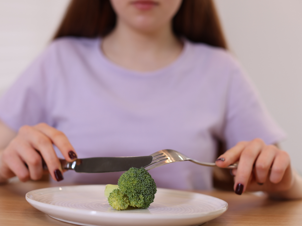 Closeup of teenage girl with broccoli on plate