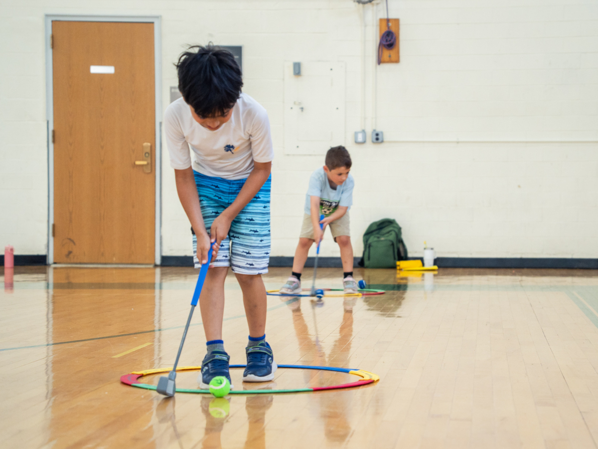 Two campers practicing golf inside the gymnasium. 