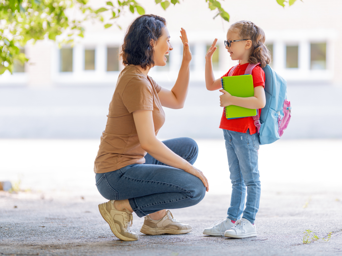Parent giving young student wearing a backpack a high five