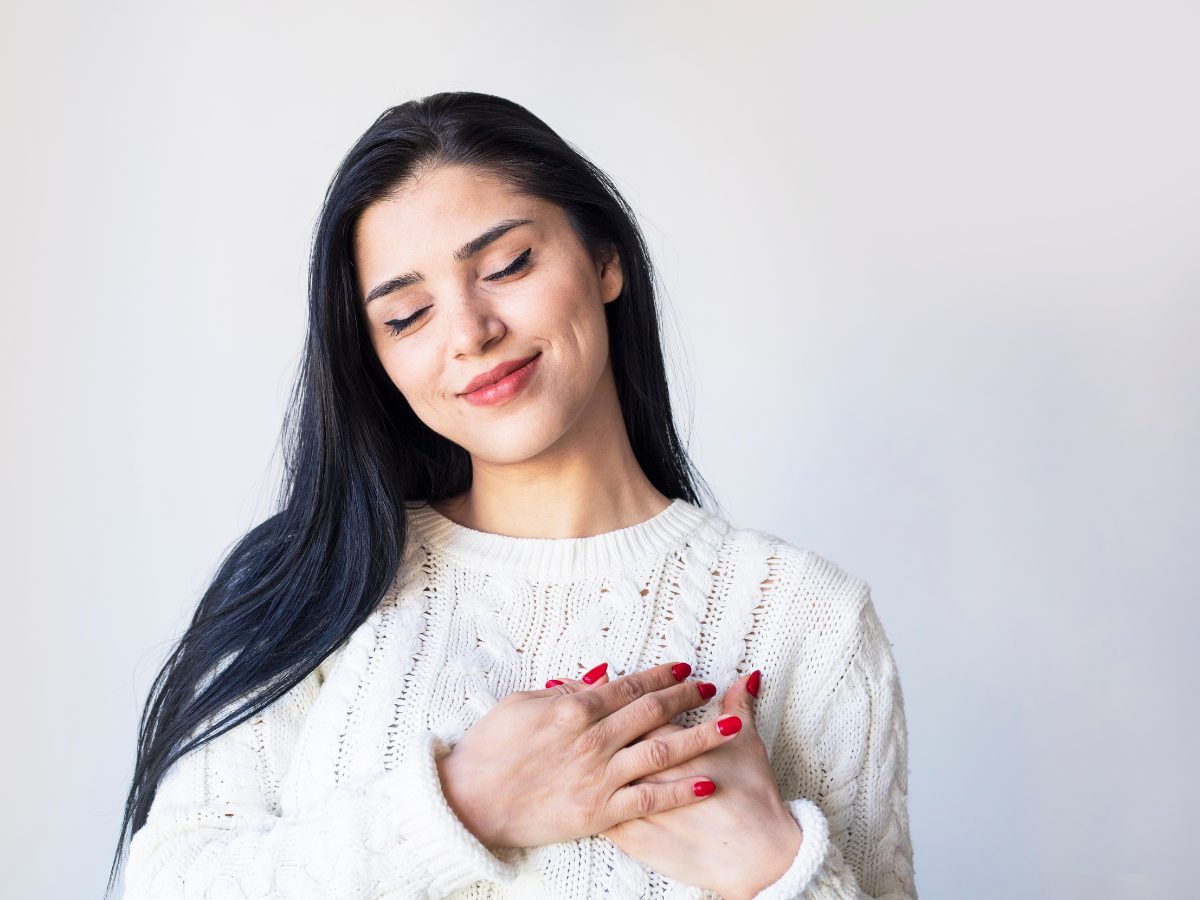 self love, acceptance, happiness. Woman with her hands over her heart, smiling.