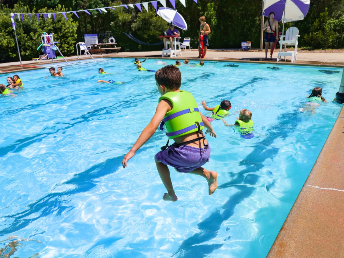 Boy wearing a lifejacket jumps into the pool.