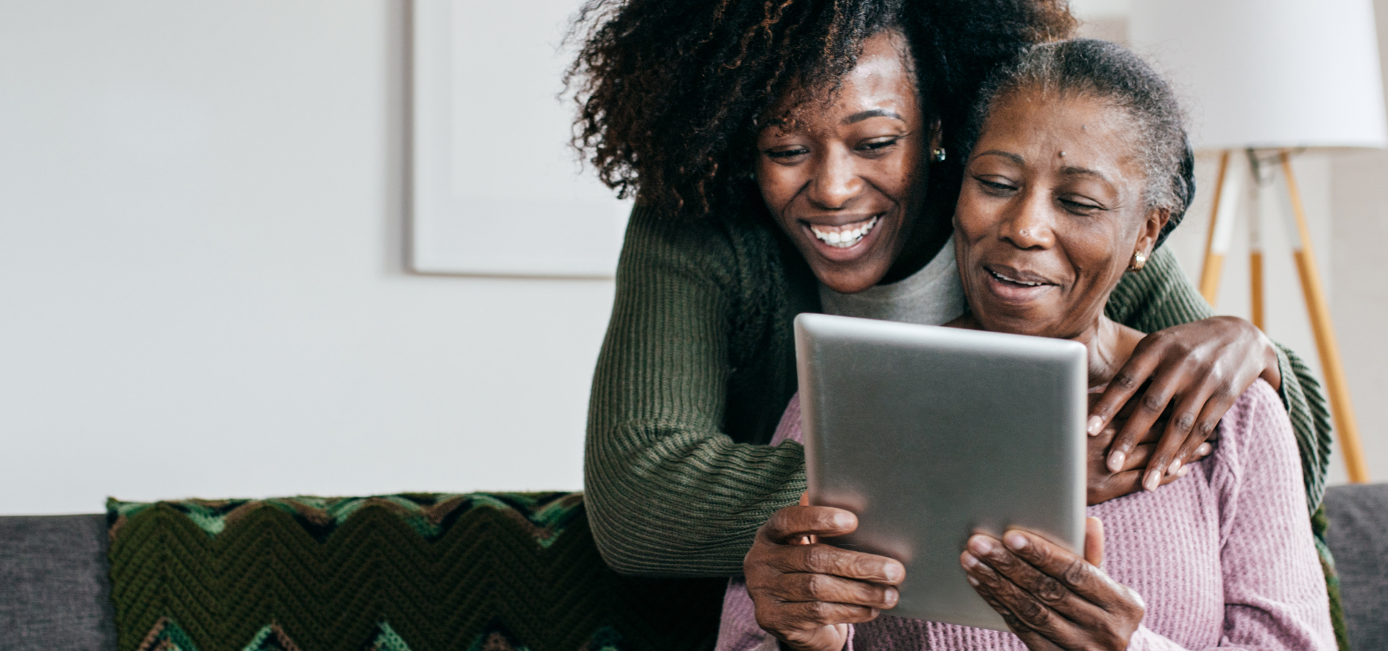 Young woman embraces an older woman holding a tablet.