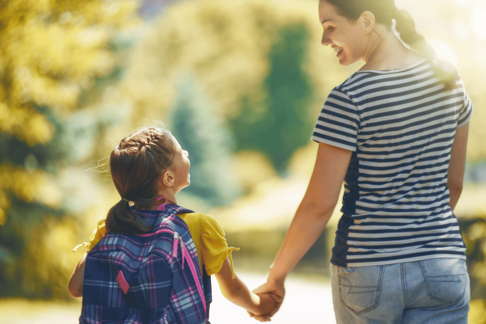 Woman holds hands with child wearing a backpack.